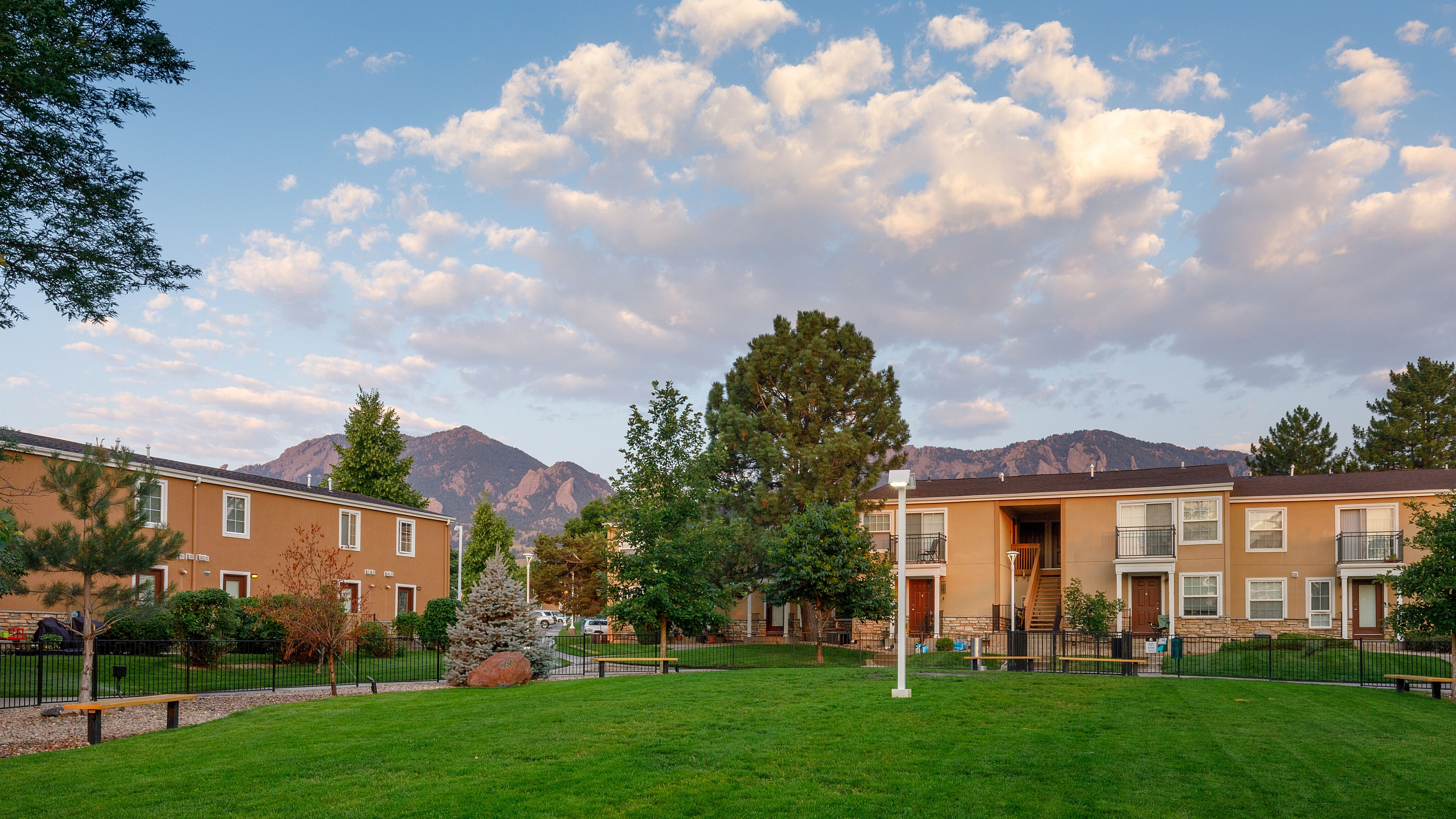 Charming apartment complex surrounded by lush greenery and framed by stunning mountain views under a vibrant blue sky.
