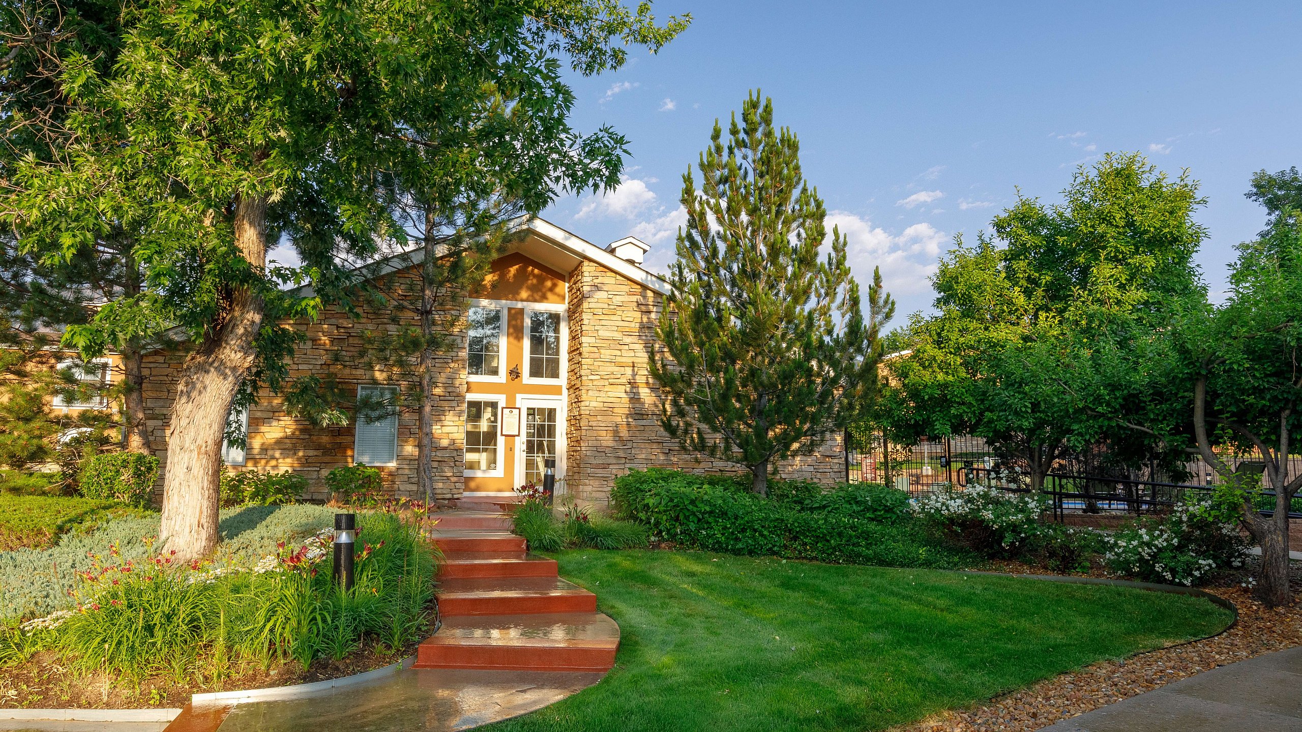 Charming stone house surrounded by lush greenery and vibrant landscaping under a clear blue sky.