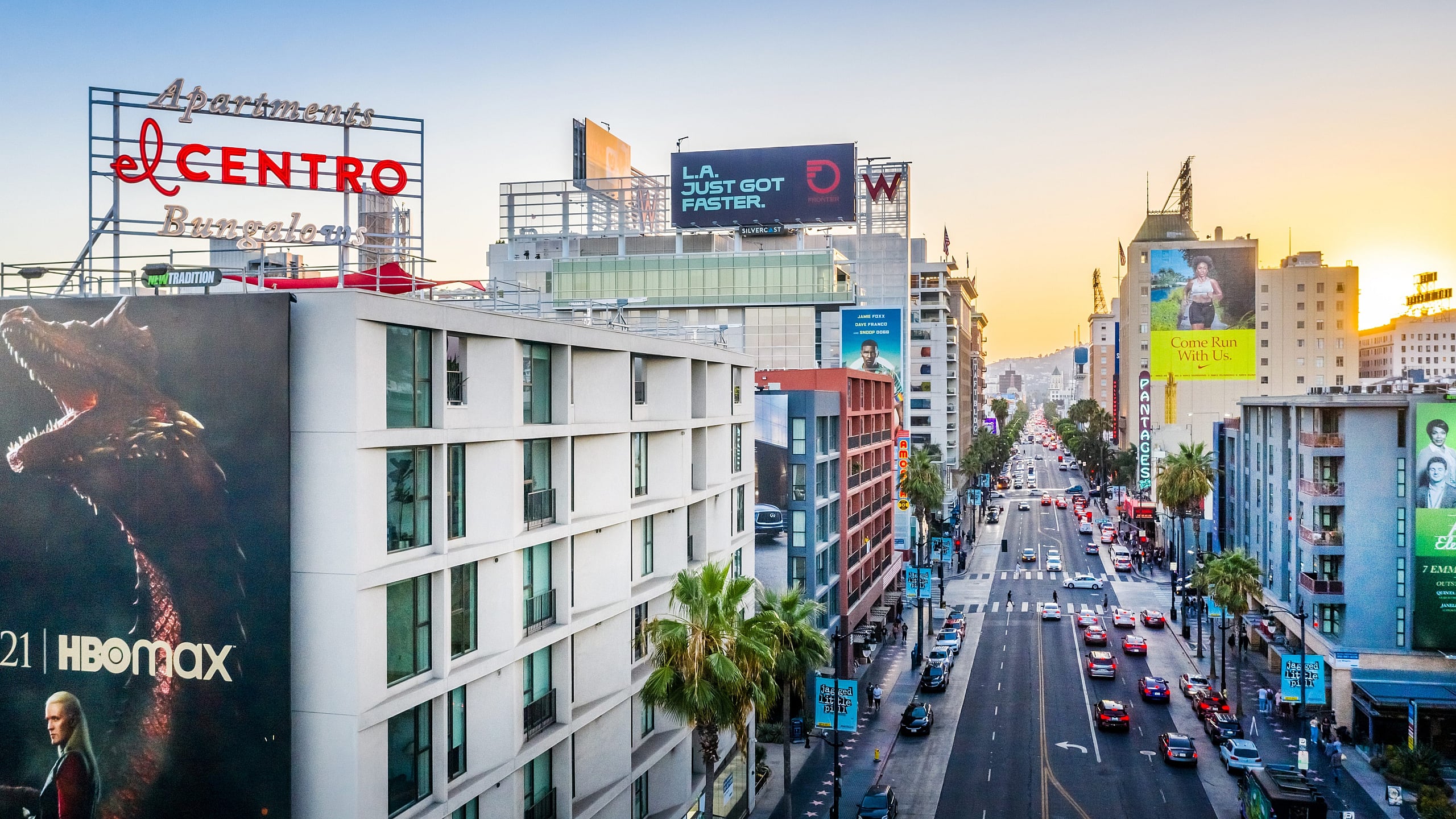 Vibrant cityscape view featuring modern El Centro apartments with bustling streets and towering billboards at sunset.