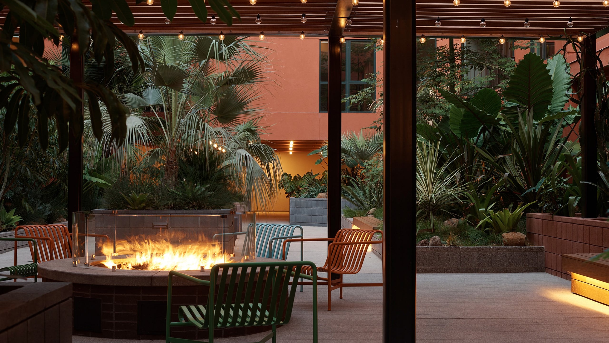 Chic outdoor patio with stylish seating around a cozy fire pit, surrounded by lush tropical plants and ambient string lighting.