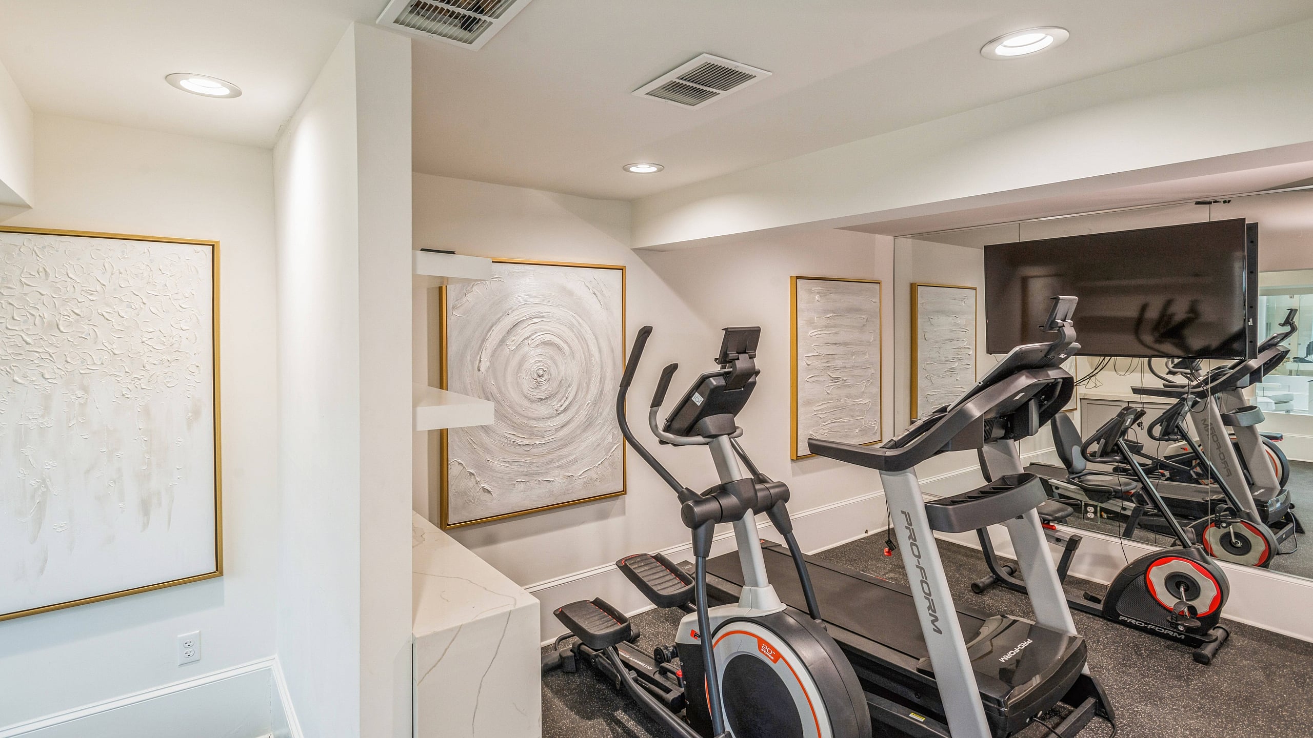 Modern home gym with exercise equipment, stylish artwork, and mirrored walls for a sleek workout space.