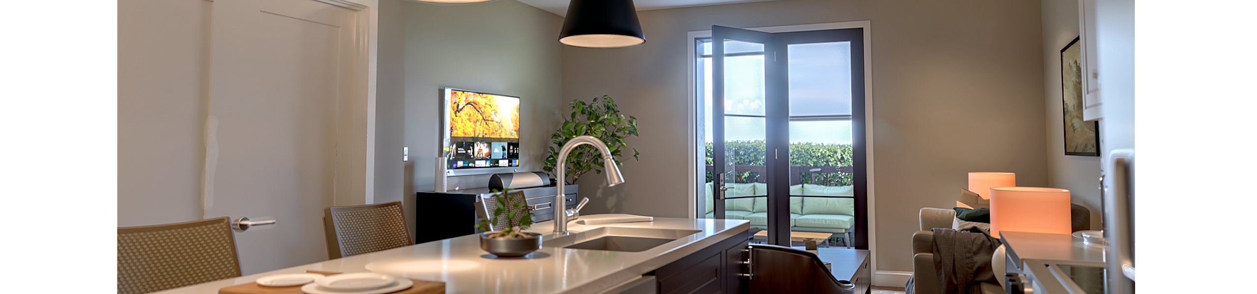 Modern kitchen and living area with sleek countertops, stylish pendant lighting, and a cozy seating space opening to a spacious balcony.