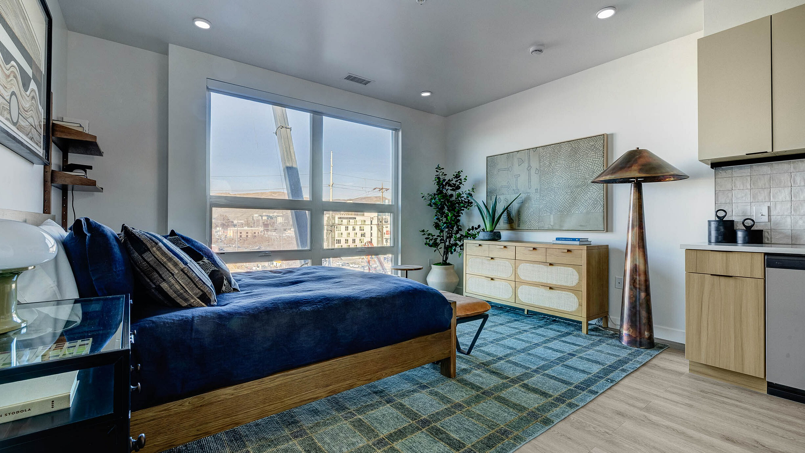 Modern apartment interior with large windows, cozy bed, stylish rug, and elegant decor.