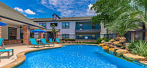 Gorgeous apartment community with a sparkling blue pool, sun loungers, and lush landscaping under a vibrant blue sky.