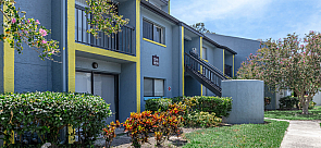 Charming apartment exterior with vibrant landscaping, featuring a modern blue facade with yellow accents and private balconies.