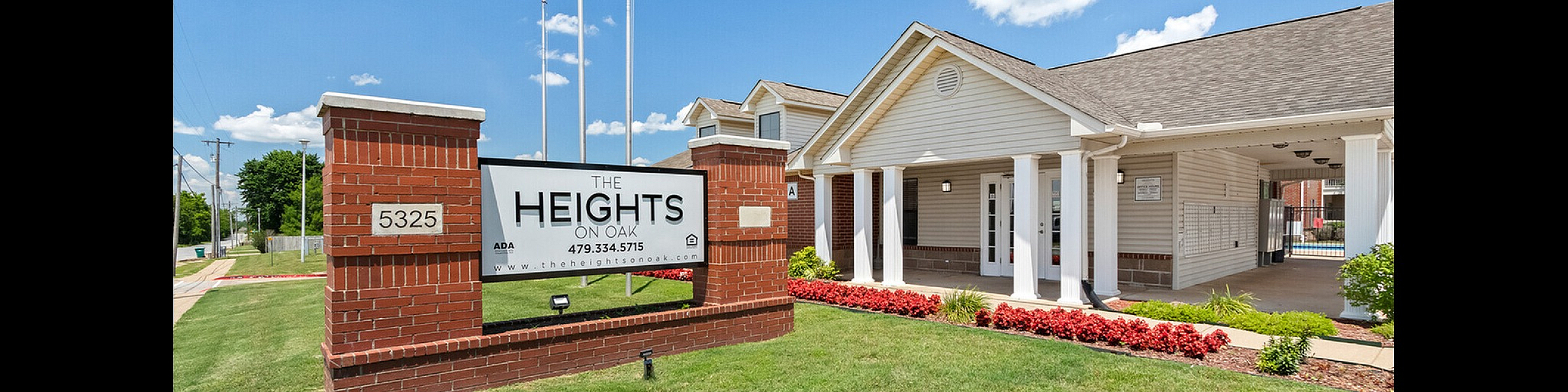 Welcoming entrance of The Heights on Oak showcasing a charming building with elegant columns and lush landscaping under a vibrant blue sky.