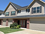 Charming duplex with modern architecture, featuring a neatly manicured lawn and spacious double garages under a clear blue sky.