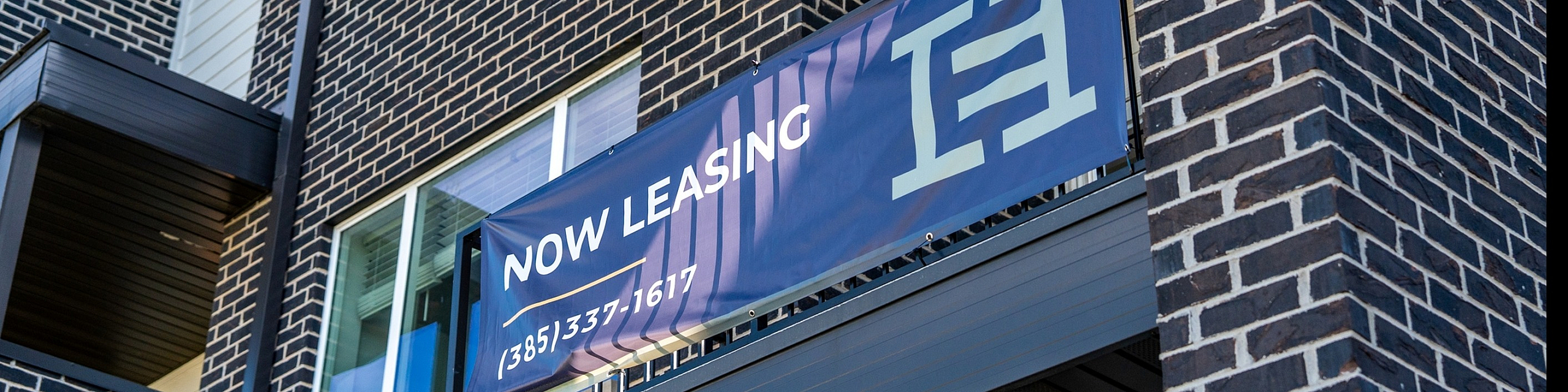 Modern townhome exterior with a now leasing banner, showcasing stylish brickwork and large windows.