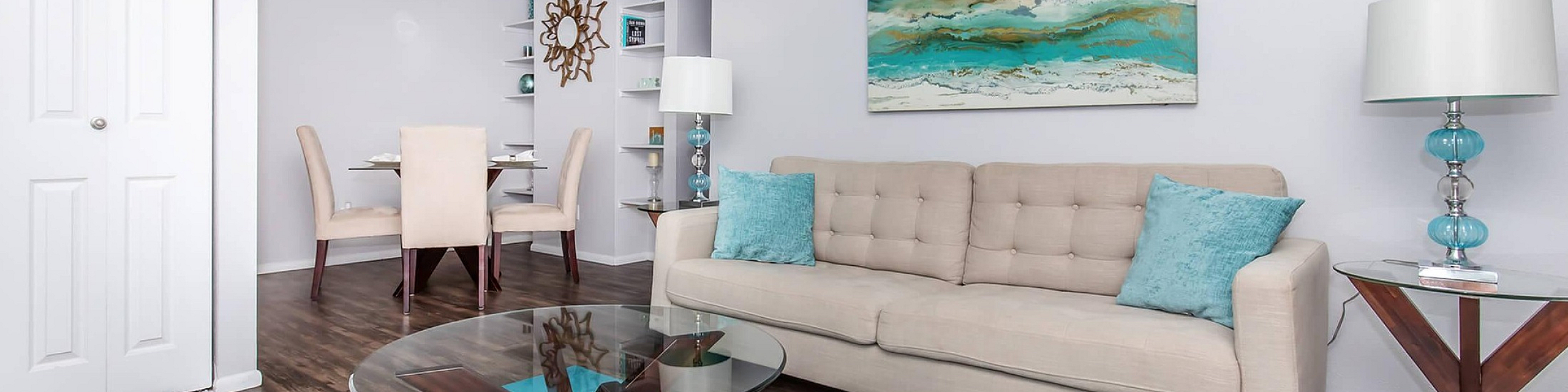 Bright, modern living room with stylish decor, featuring a cozy beige sofa, glass coffee table, and vibrant turquoise accents for a fresh, inviting atmosphere.