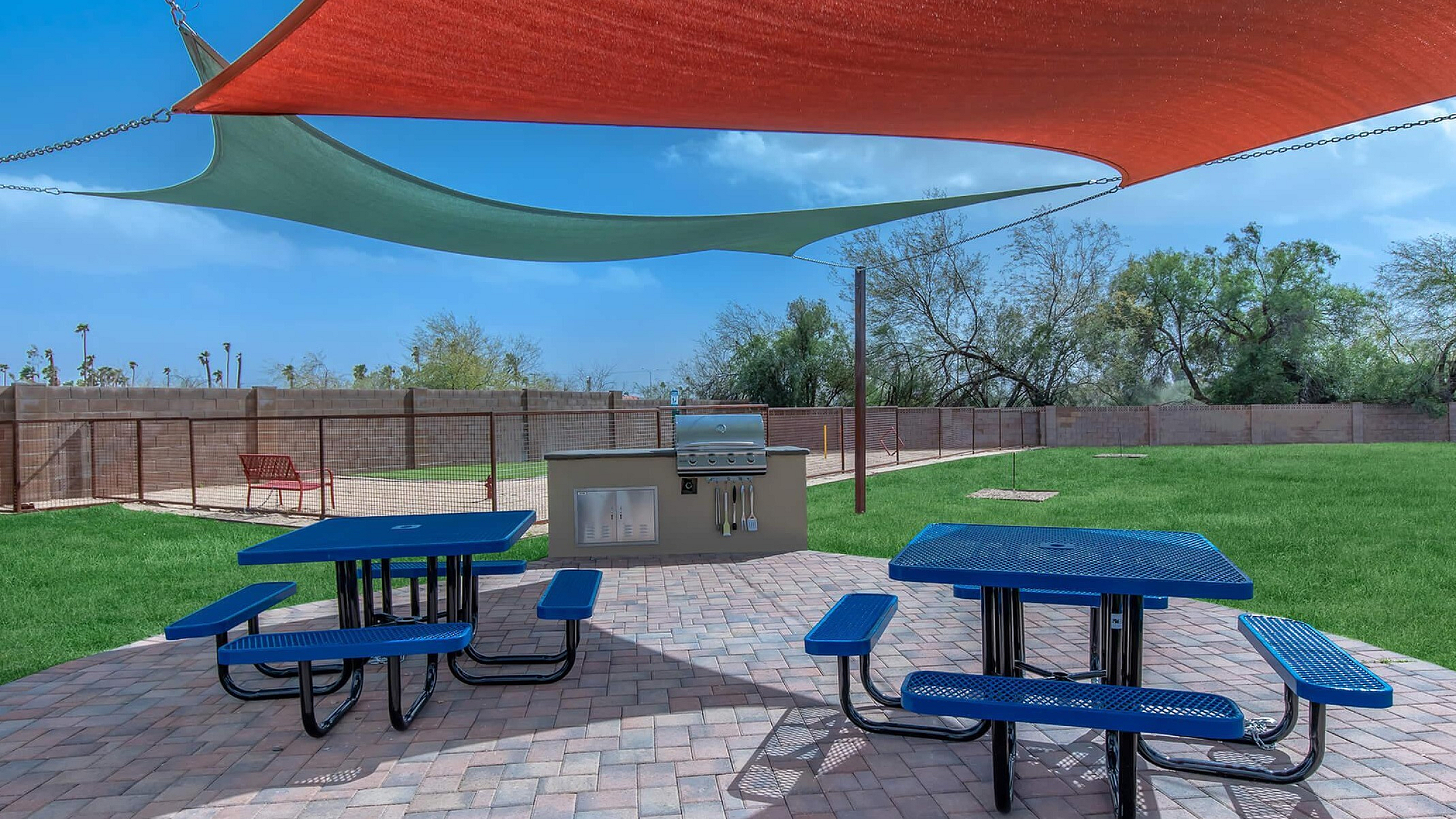 Charming outdoor area featuring vibrant shade sails, modern picnic tables, and a state-of-the-art BBQ grill on a spacious patio.