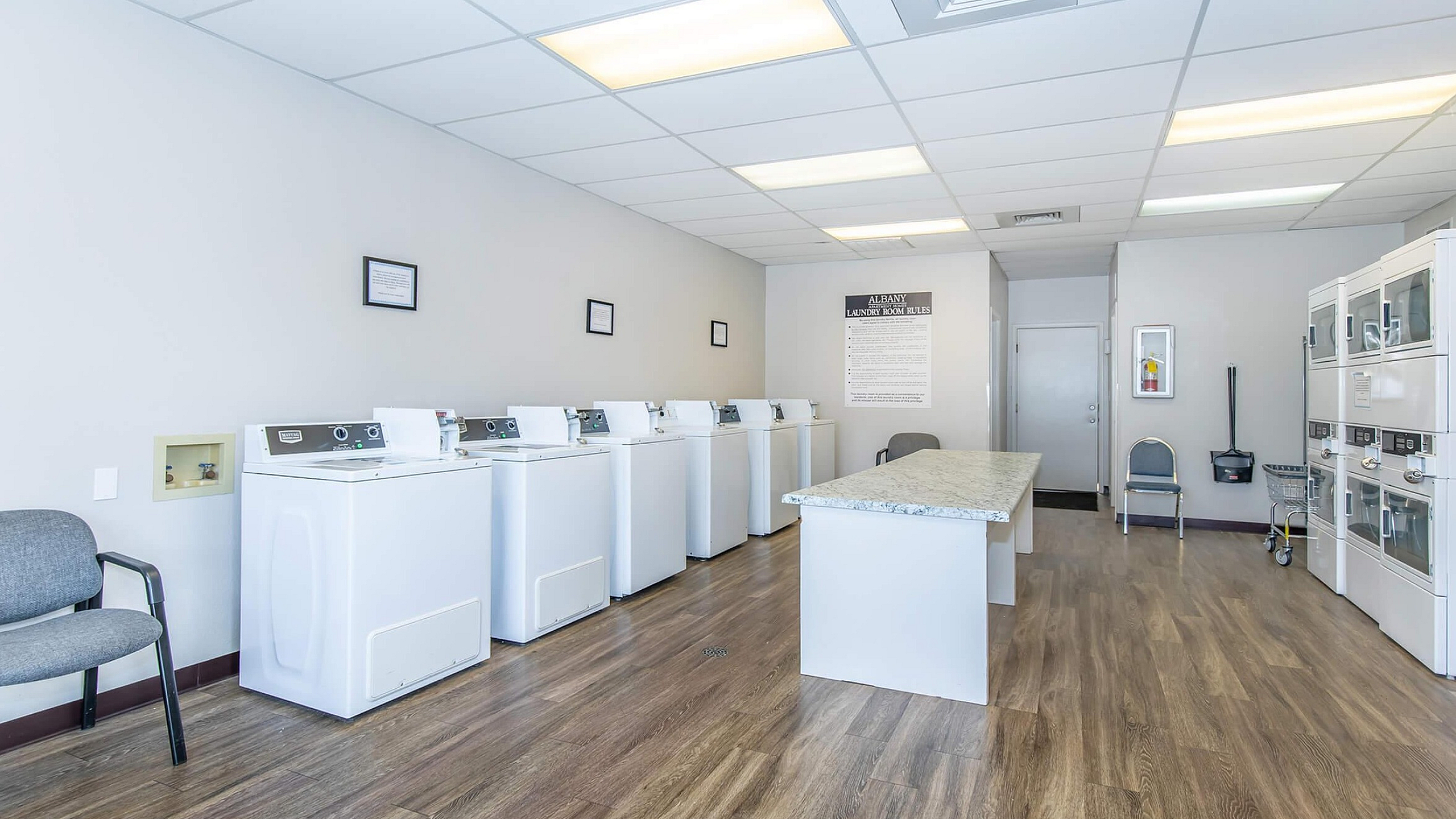 Bright and spacious laundry facility with modern washing machines, ample folding space, and sleek wood flooring.