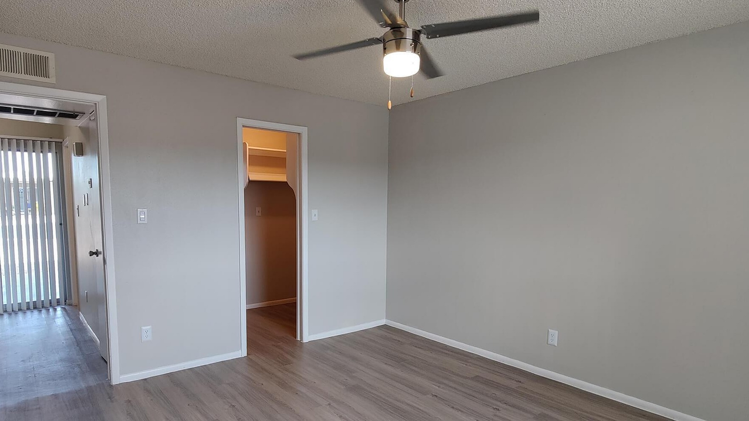 Spacious bedroom with elegant laminate flooring, ceiling fan, and ample natural light from glass doors, offering a tranquil and airy atmosphere.