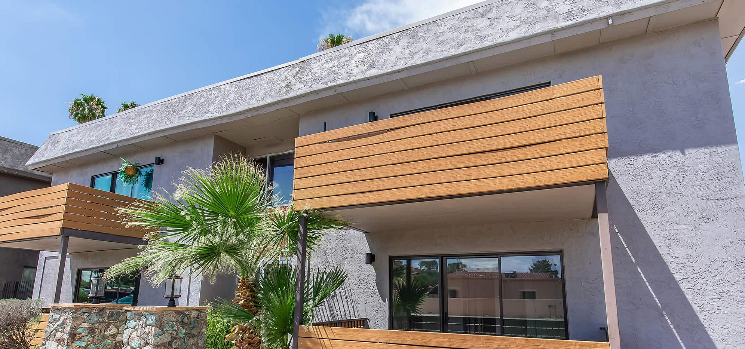 Modern apartment exterior with stylish wood paneling and lush palm trees under a clear blue sky.