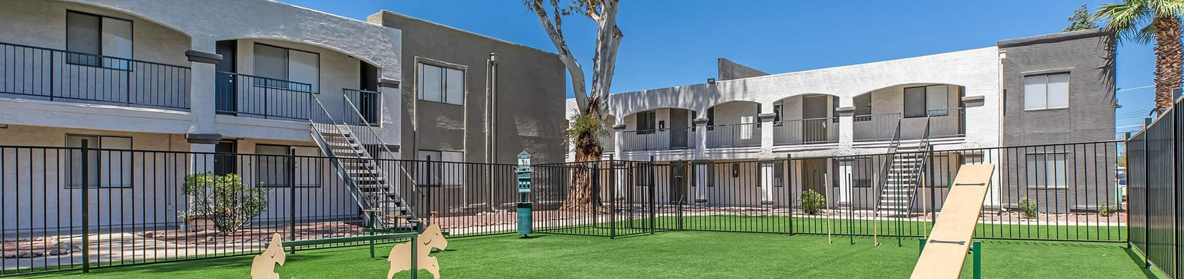 Inviting apartment complex with a vibrant green dog park, complete with agility features and spacious outdoor area.