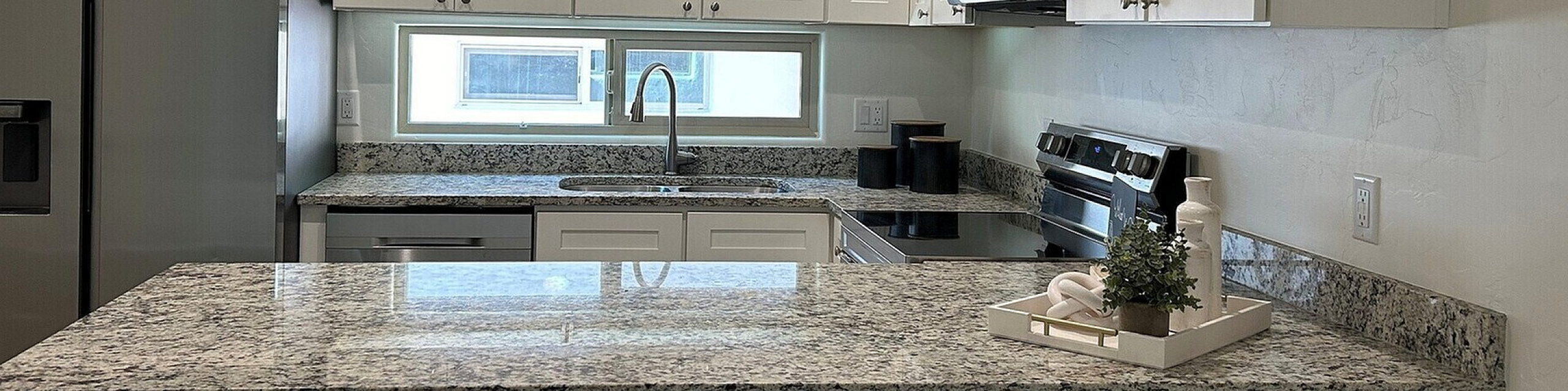 Modern kitchen with sleek granite countertops, stainless steel appliances, and elegant white cabinetry, perfect for culinary adventures.