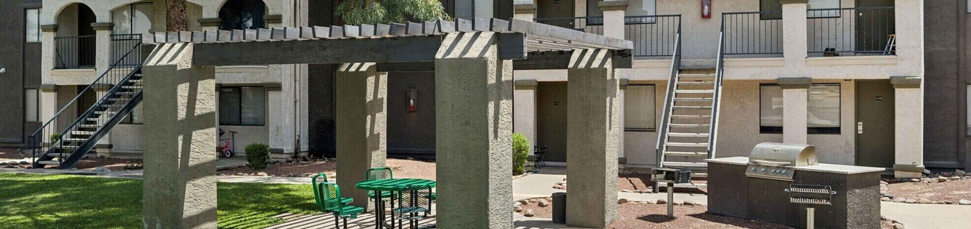 Charming apartment exterior with lush green lawn, pergola with picnic seating, and built-in barbecue station for outdoor enjoyment.