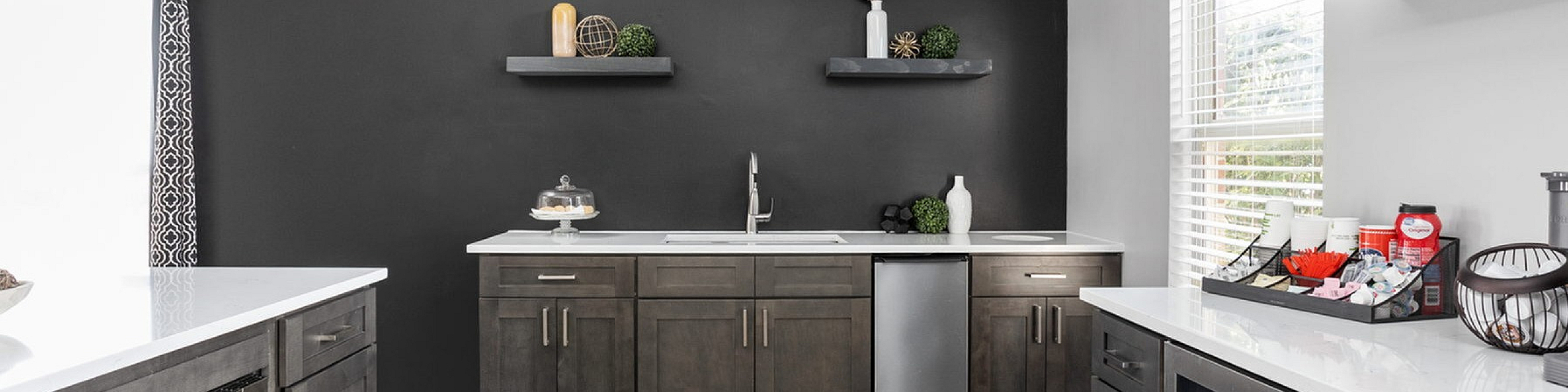 Modern kitchen with sleek black cabinets, stainless steel appliances, and elegant open shelving, complemented by a stylish black accent wall and warm wood flooring.