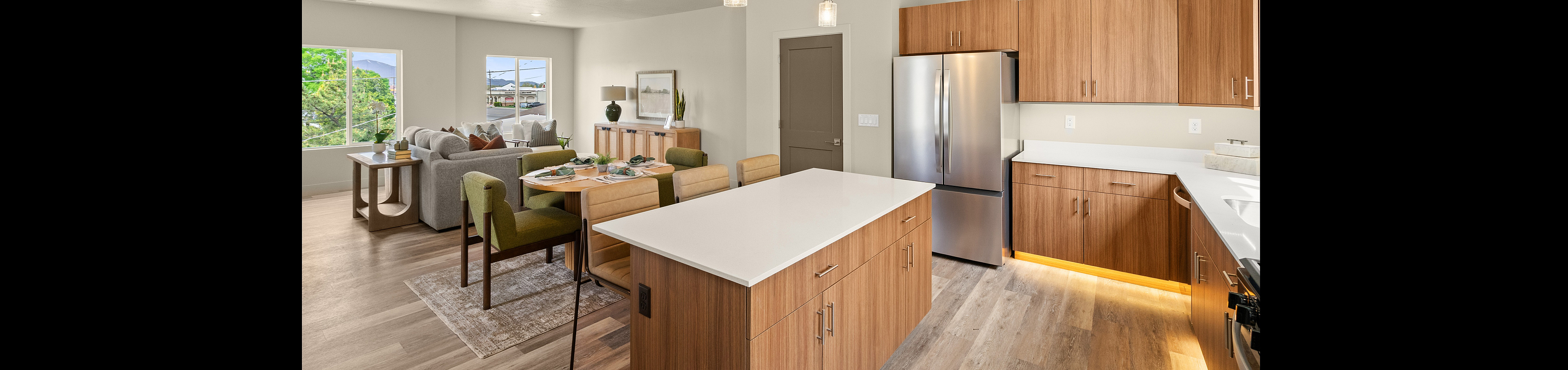 Contemporary open-plan kitchen and dining area with sleek wood cabinetry, a large island, and modern stainless steel appliances, leading into a bright living room with elegant d&eacute;cor and large windows.