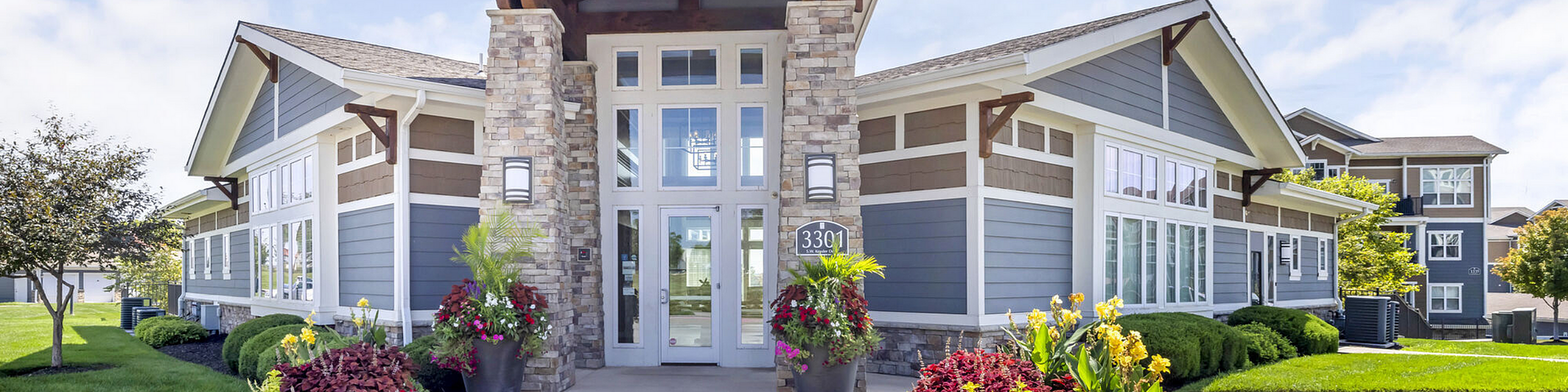 Charming modern apartment complex with stone accents, lush landscaping, and inviting entryway.