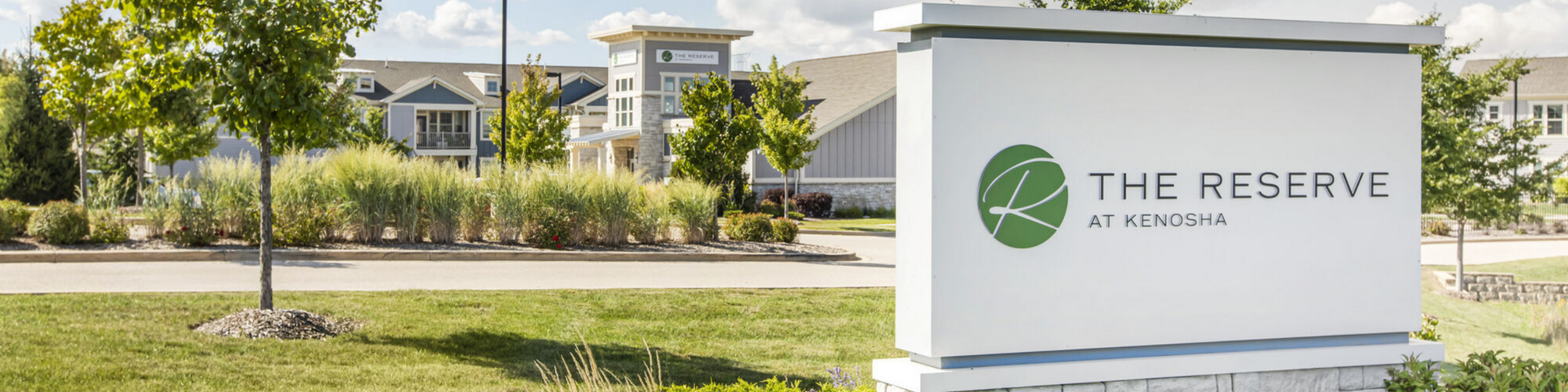 Charming entrance of The Reserve at Kenosha with lush landscaping and elegant signage.