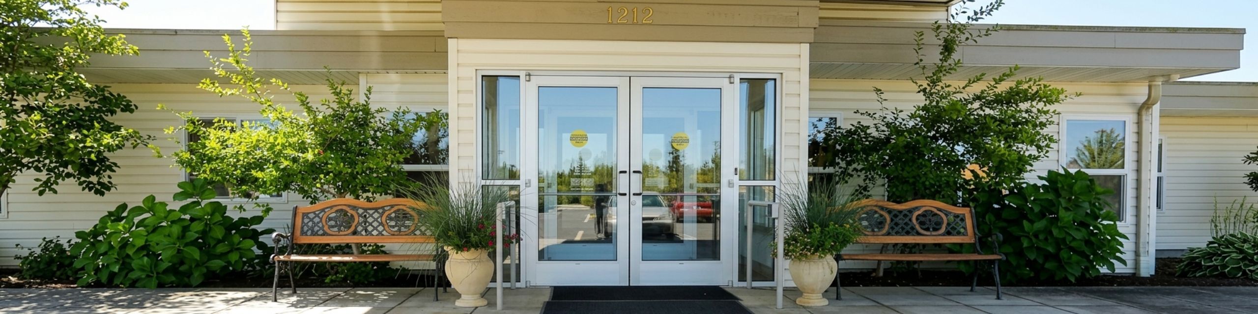 Inviting apartment entrance surrounded by lush greenery and elegant benches, offering a welcoming atmosphere.