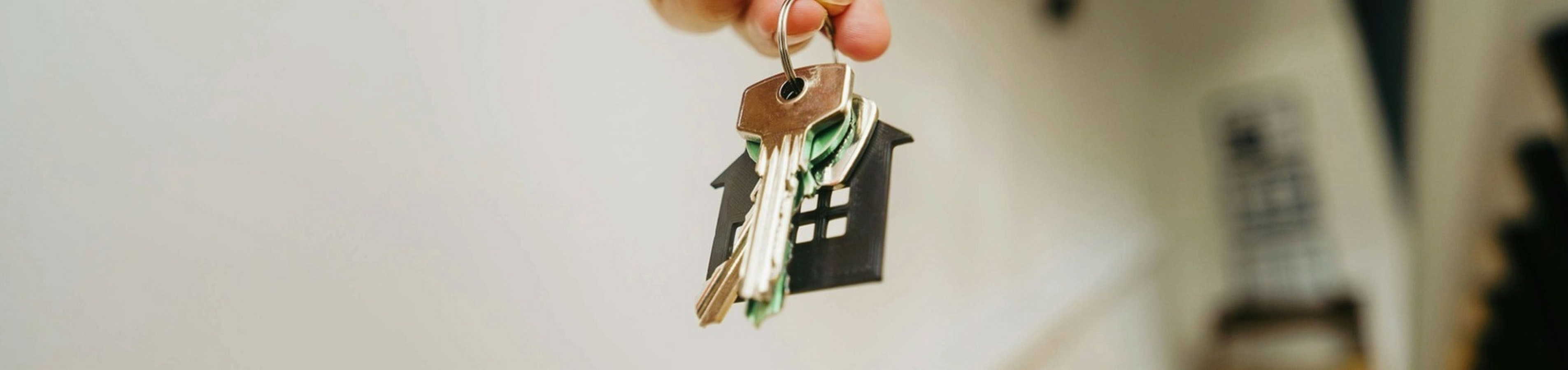 Close-up of a hand holding house keys with a staircase in the background, symbolizing a new home opportunity.