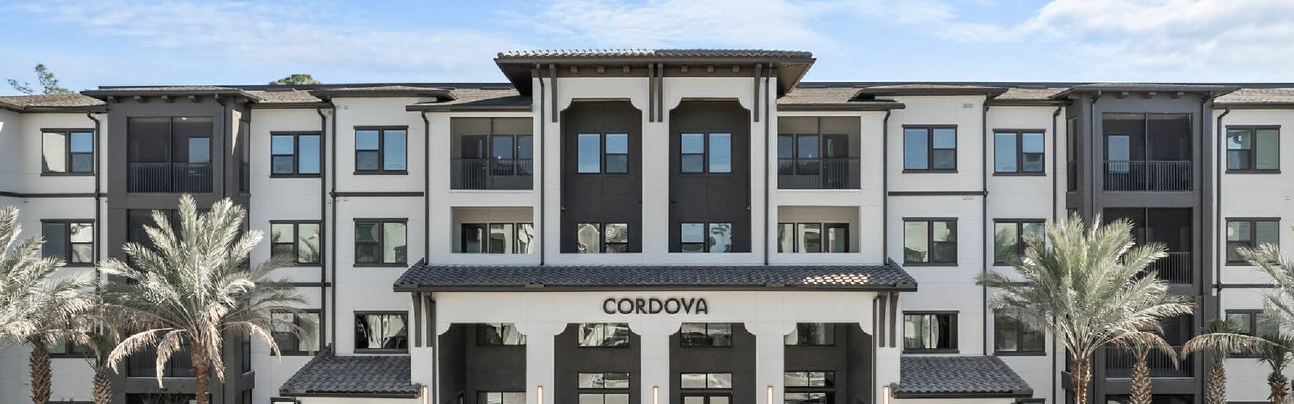 Elegant modern apartment building with palm trees and a grand entrance under a vibrant blue sky.