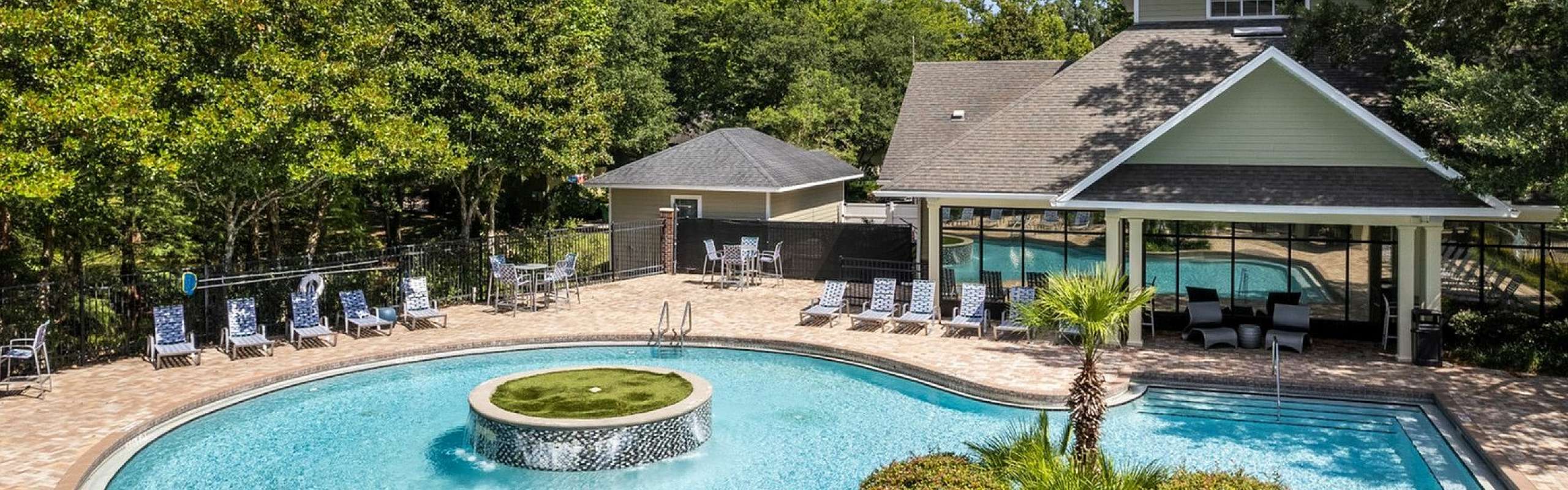 Luxurious outdoor pool area surrounded by lush greenery, featuring stylish seating and a unique central fountain for a perfect retreat ambience.