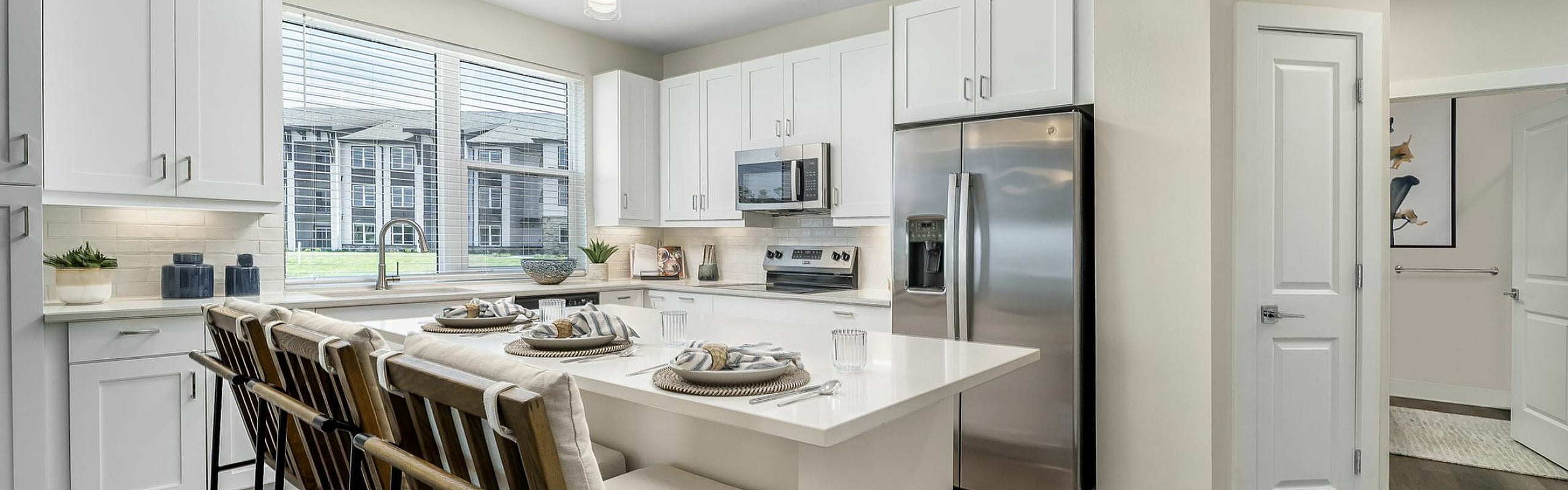 Modern kitchen with sleek white cabinetry, large island with stylish seating, stainless steel appliances, and ample natural light.