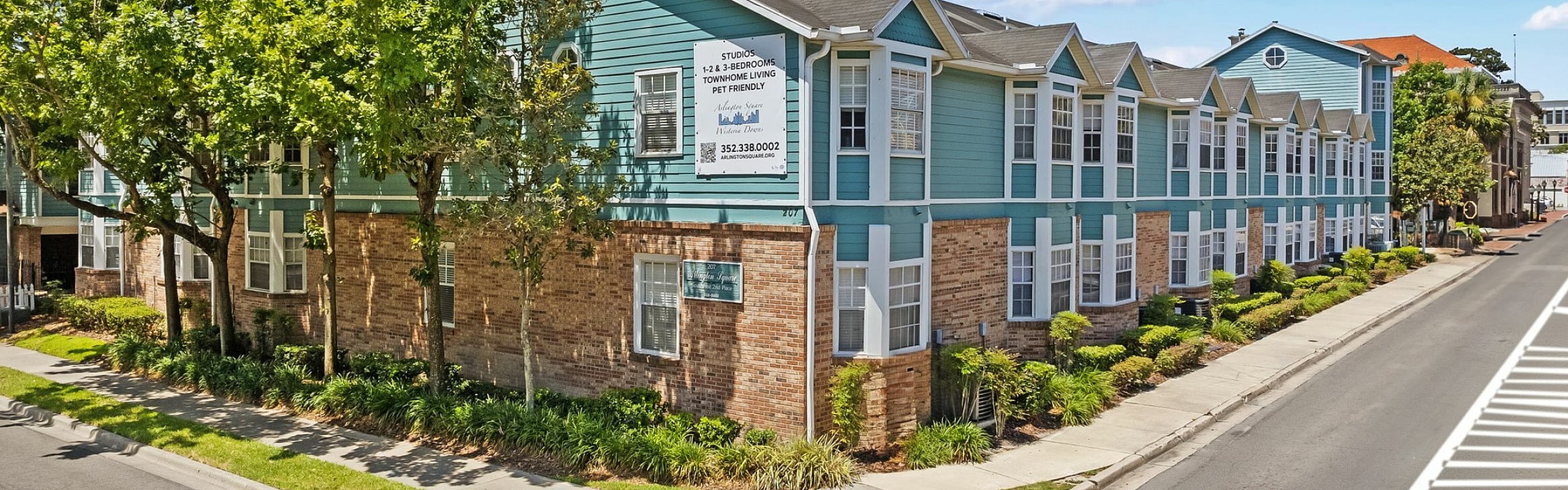 Charming apartment complex with modern blue and brick exterior, lush green landscaping, and pet-friendly environment.