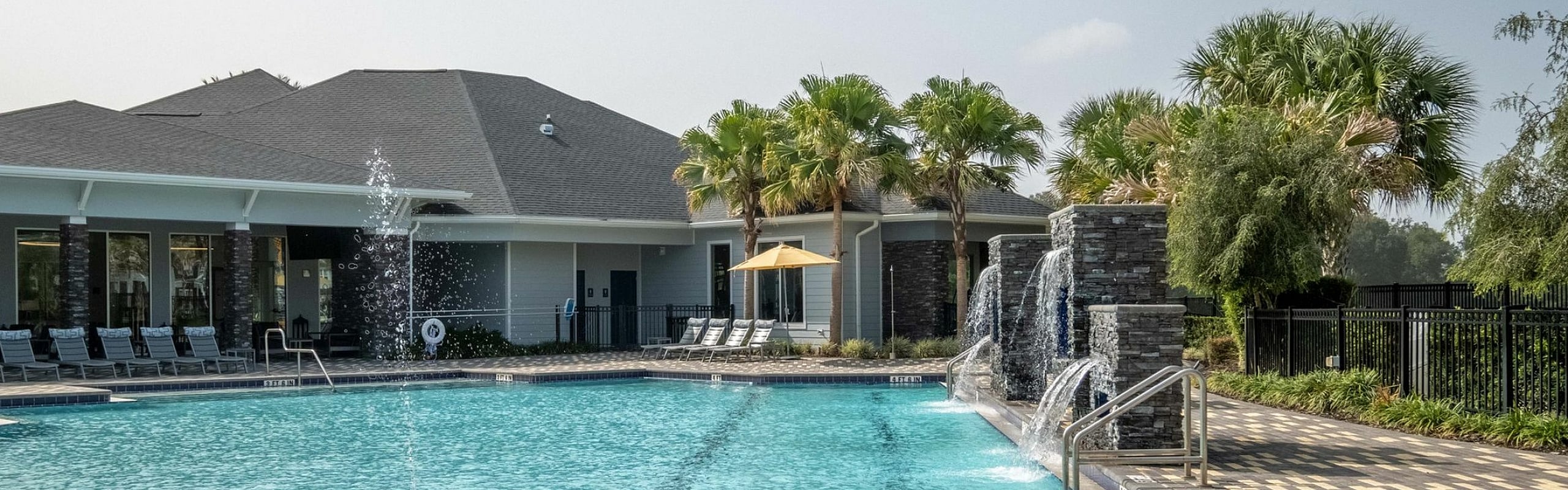 Luxurious apartment community featuring a stunning swimming pool with cascading waterfalls and lush palm trees.