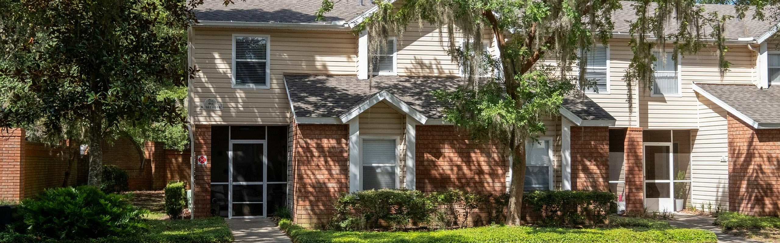 Charming townhouse nestled in a lush, green setting with brick accents and ample parking space.