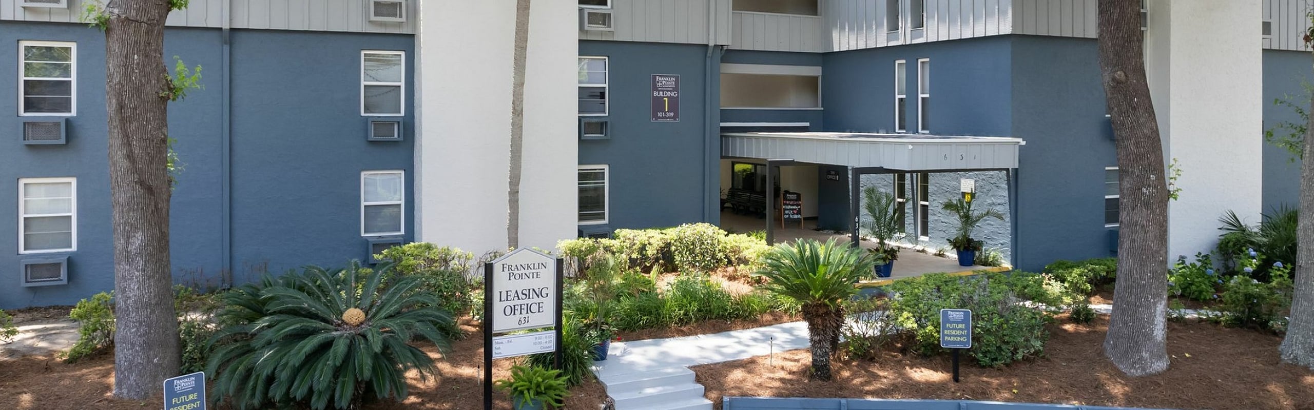Charming apartment complex with modern design, lush landscaping, and convenient leasing office under a clear blue sky.