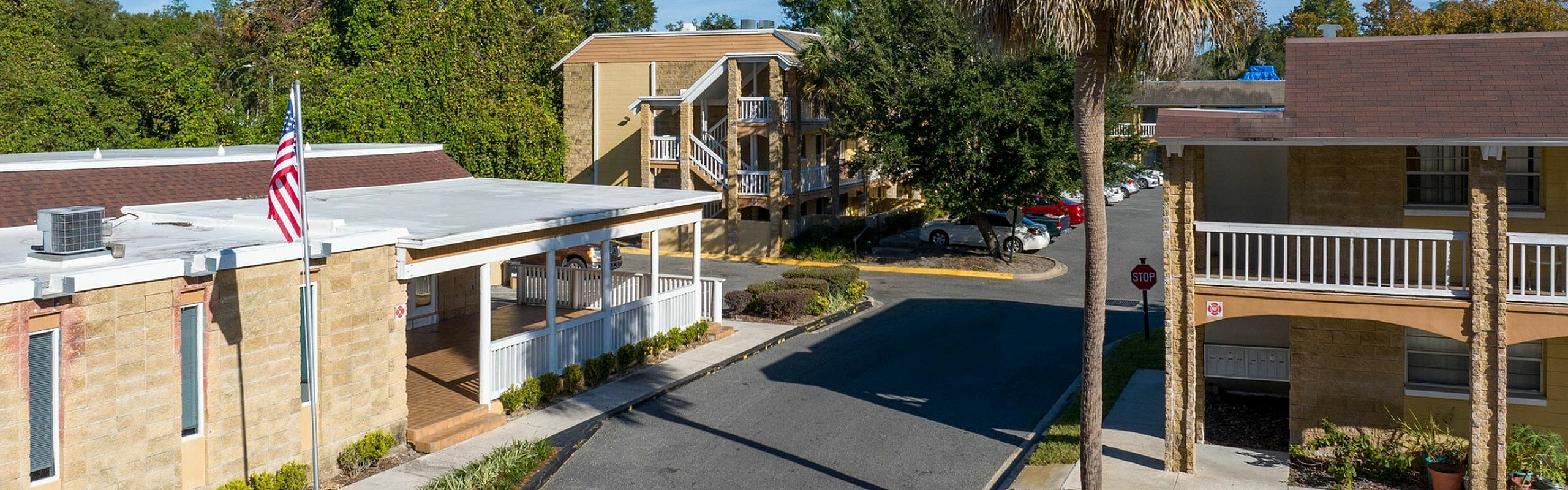 Charming apartment complex with beige buildings, vibrant landscaping, and a welcoming entrance under a clear blue sky.