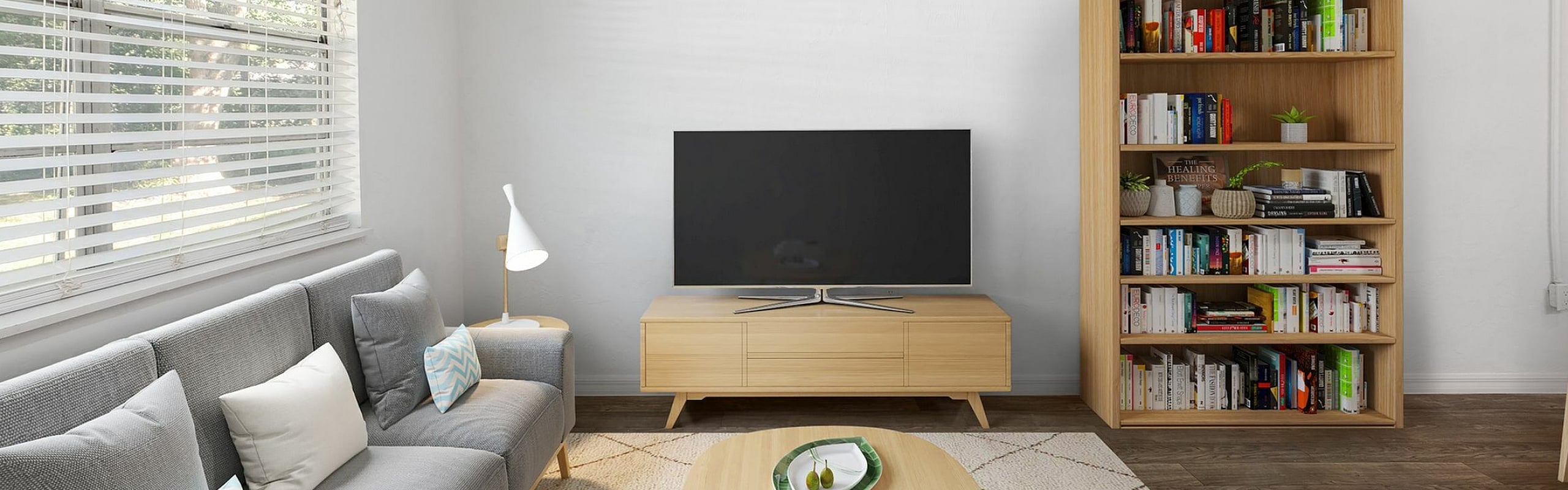 Bright and inviting living room with a sleek grey sofa, modern wooden furniture, and a well-organized bookshelf, perfect for relaxation and entertainment.