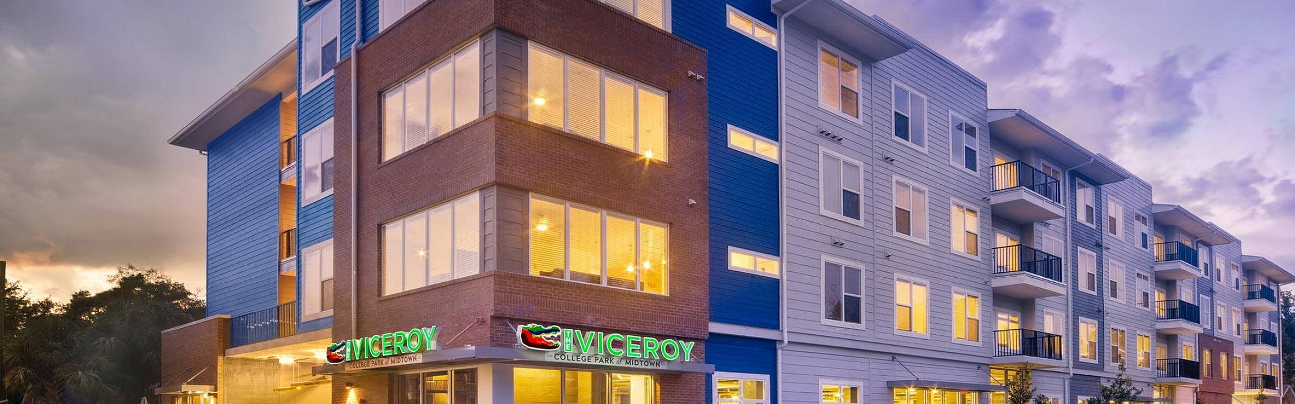 Modern apartment building with vibrant exterior lighting, showcasing sleek architectural design and inviting curb appeal at sunset.