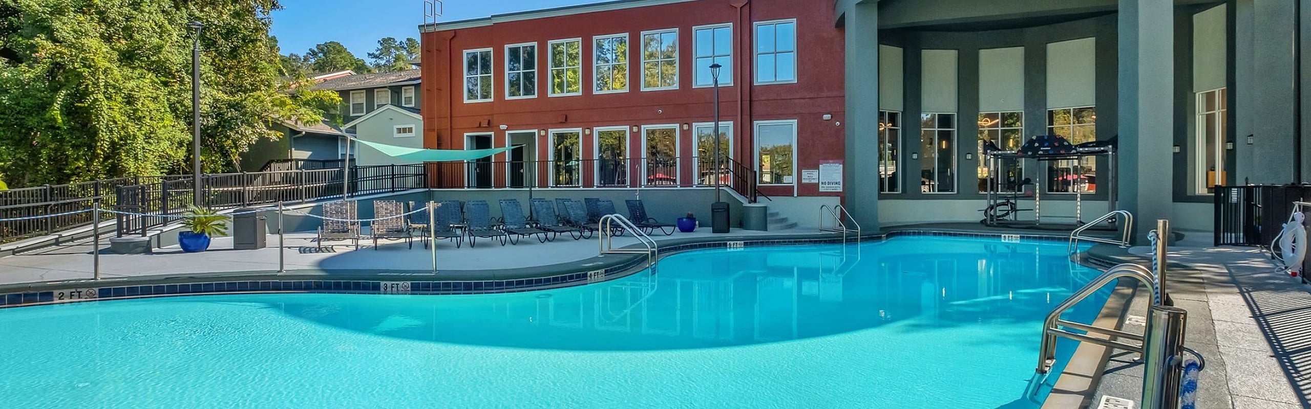 Luxurious apartment complex with a sparkling outdoor pool, surrounded by lush greenery and modern architecture.