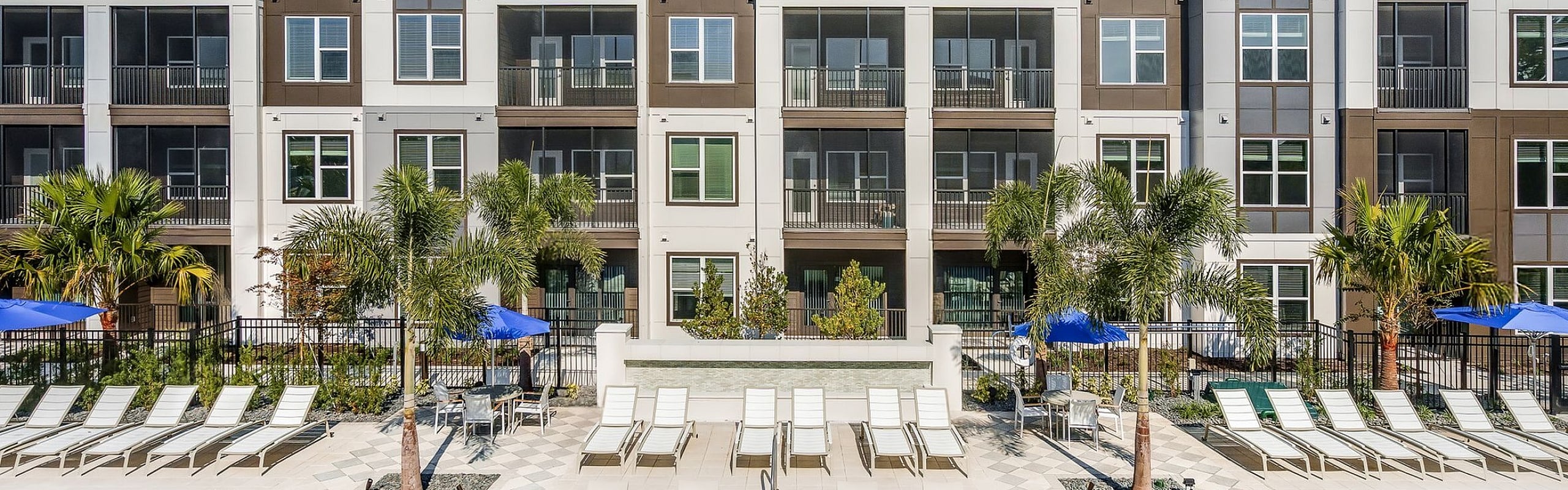 Modern apartment complex with sleek architecture and inviting pool area, featuring comfortable lounge chairs and lush palm trees.