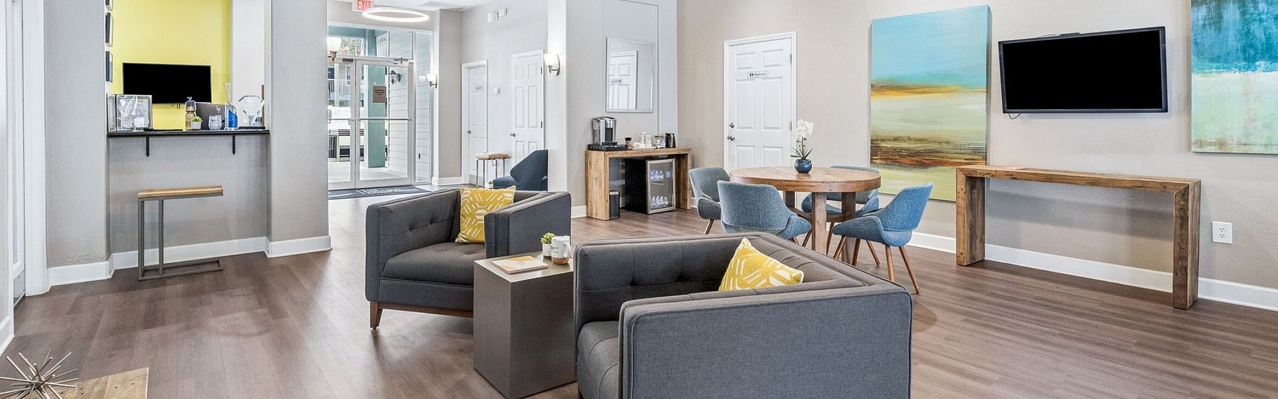 Elegant communal living space with modern gray sofas, vibrant yellow accents, and contemporary art pieces, featuring a cozy dining area and sleek wood flooring.