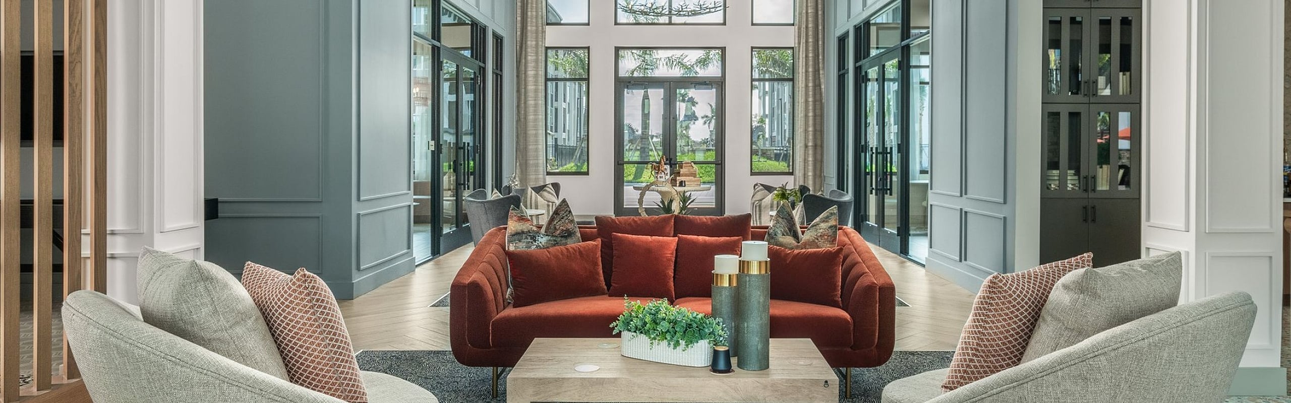 Elegant apartment lobby featuring a cozy seating area with modern furniture, vibrant red sofa, and stylish decor beneath a grand chandelier.