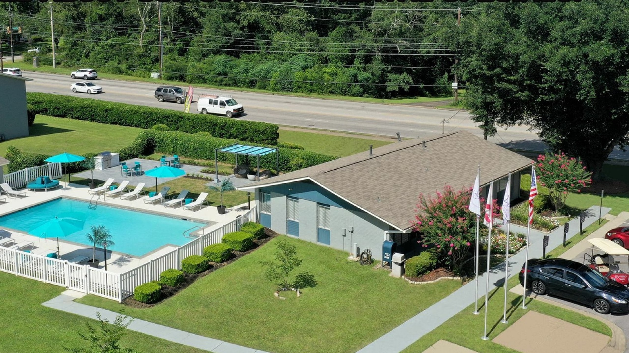 Aerial view of a beautifully landscaped apartment complex featuring a large swimming pool with lounge chairs and umbrellas.