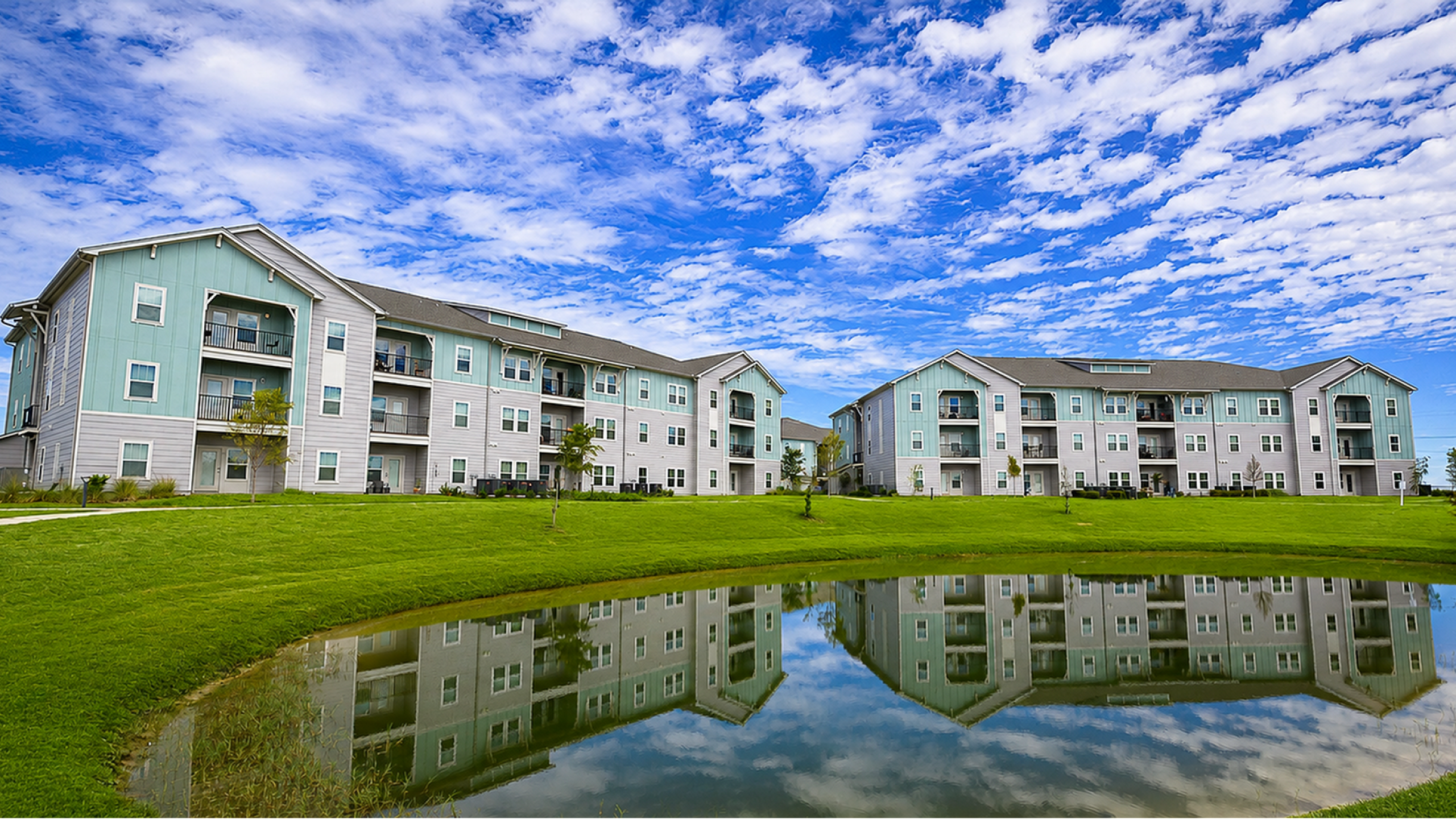 Charming residential apartment buildings with pastel exteriors, set against a beautiful sky with a serene pond reflection.