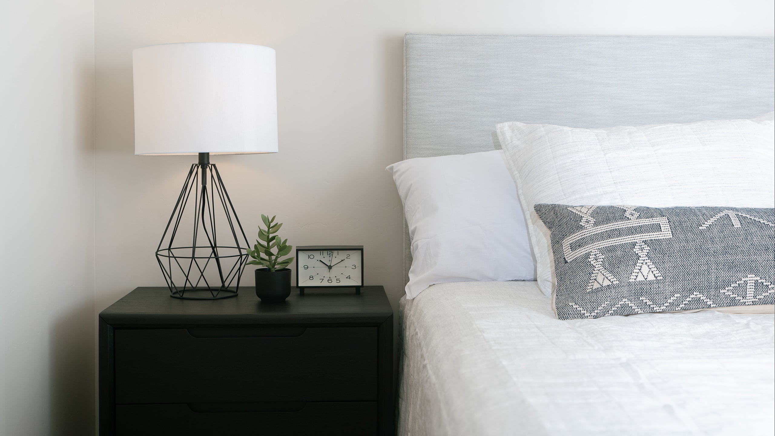 Chic bedroom corner with modern black nightstand, geometric lamp, and cozy textured bedding.