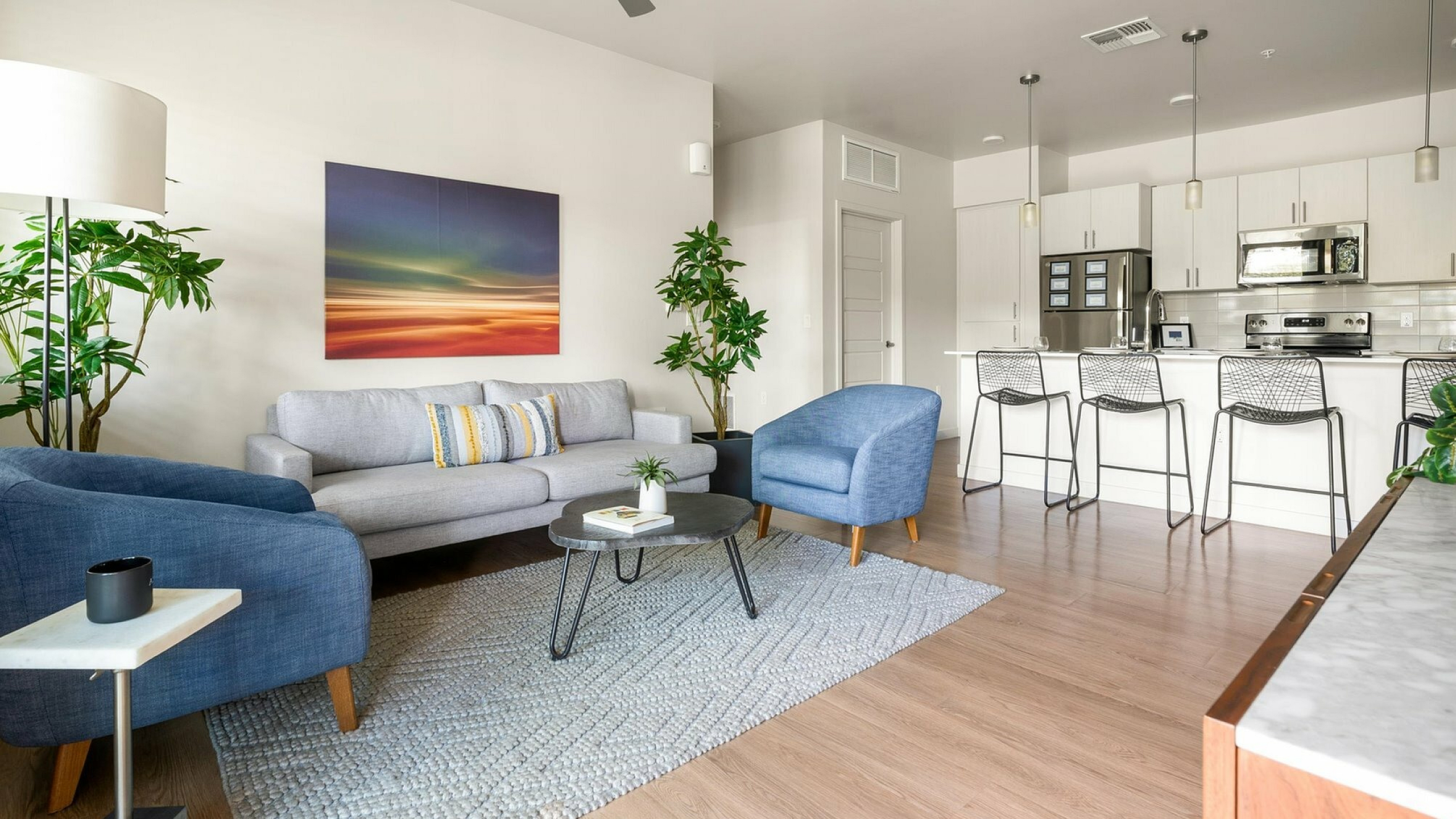 Modern open-concept living space showcasing a cozy seating area with contemporary furniture, vibrant artwork, and a sleek kitchen with bar seating.