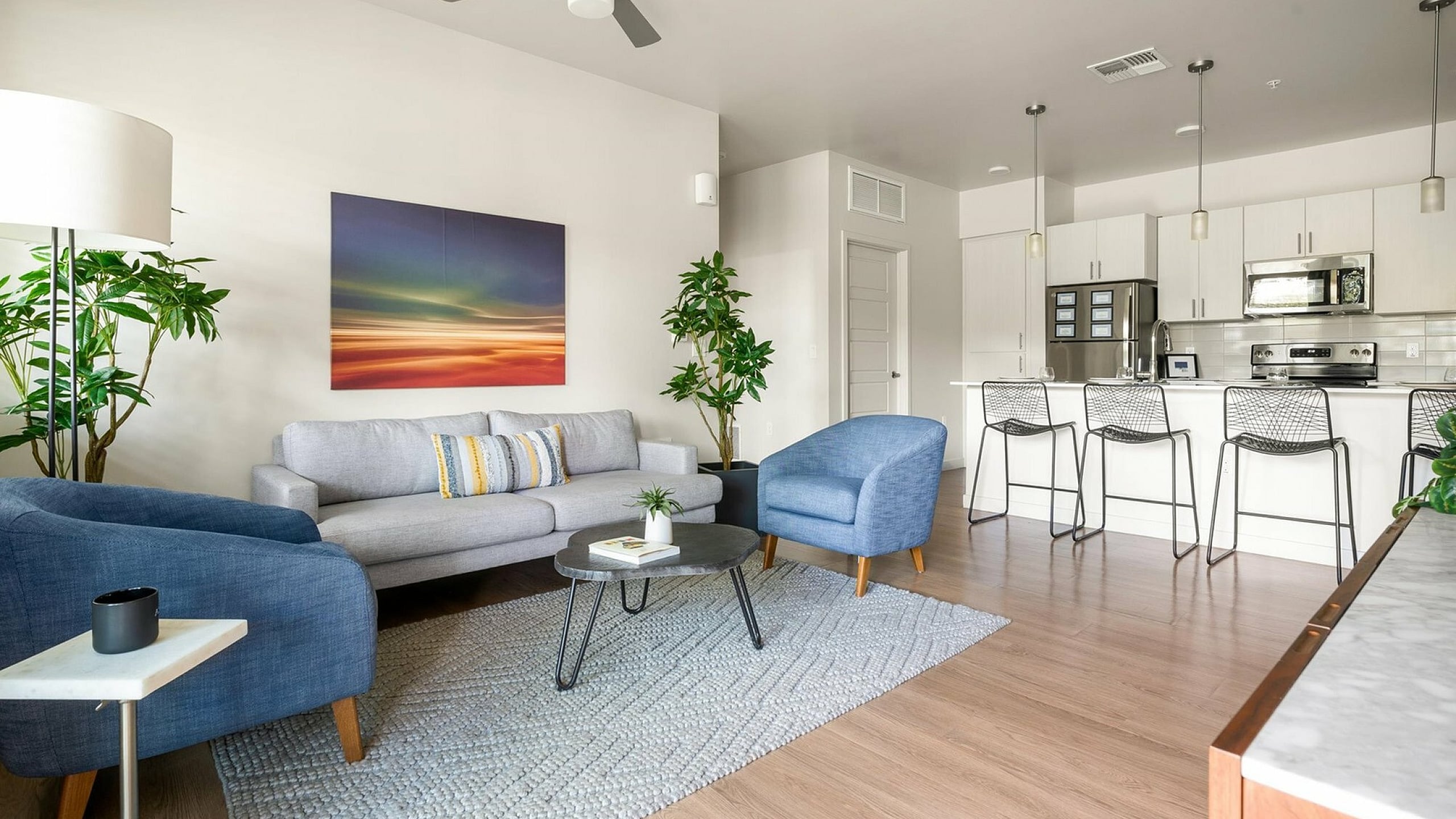 Modern open-concept living area with stylish decor, featuring a cozy grey sofa, blue armchairs, and a sleek kitchen island with bar stools.