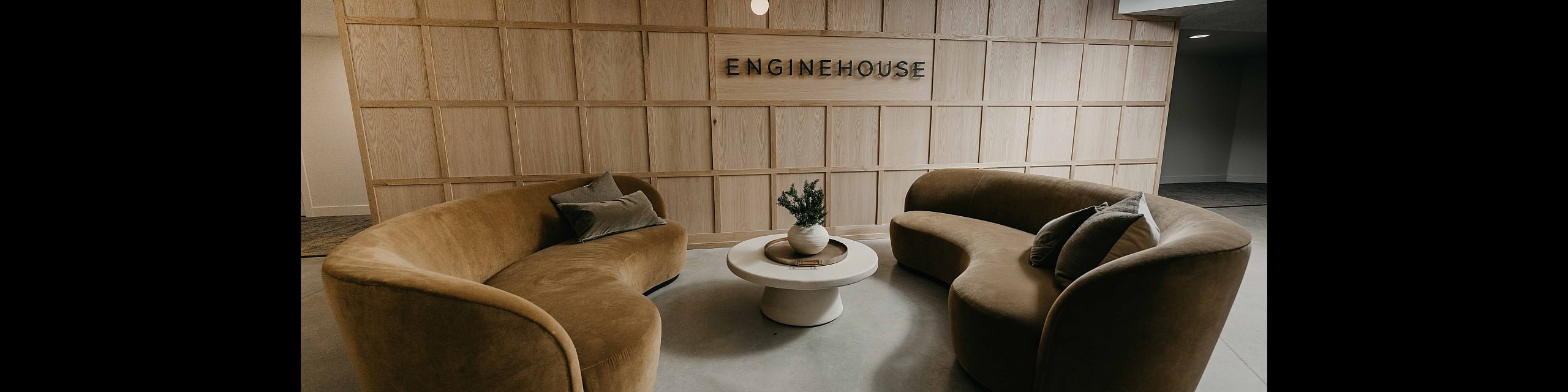 Chic lounge area at Enginehouse featuring elegant curved sofas and a modern chandelier, exuding contemporary sophistication.