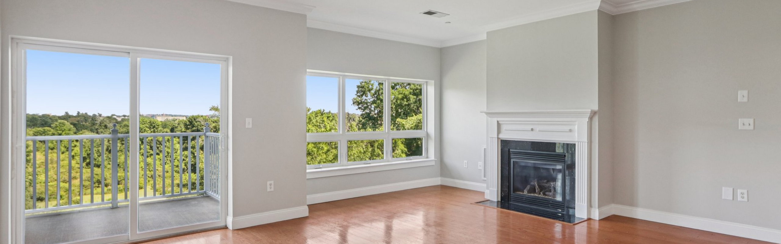 Bright living room featuring elegant fireplace, large windows, and private balcony with stunning forest views.