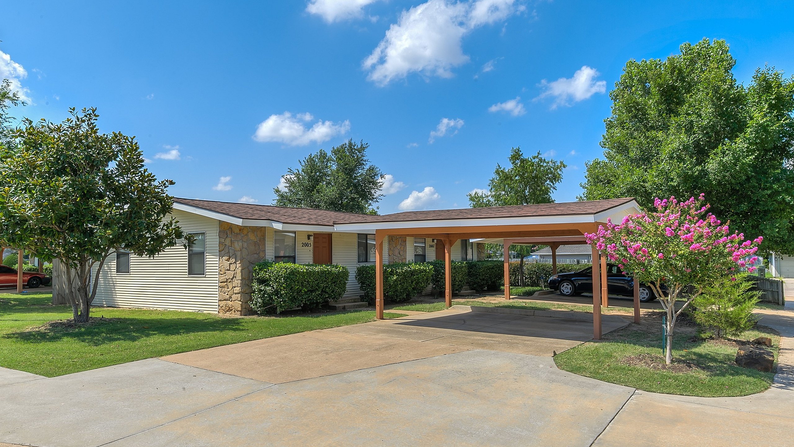 Inviting suburban home with carport, surrounded by lush greenery and a vibrant flowering tree.