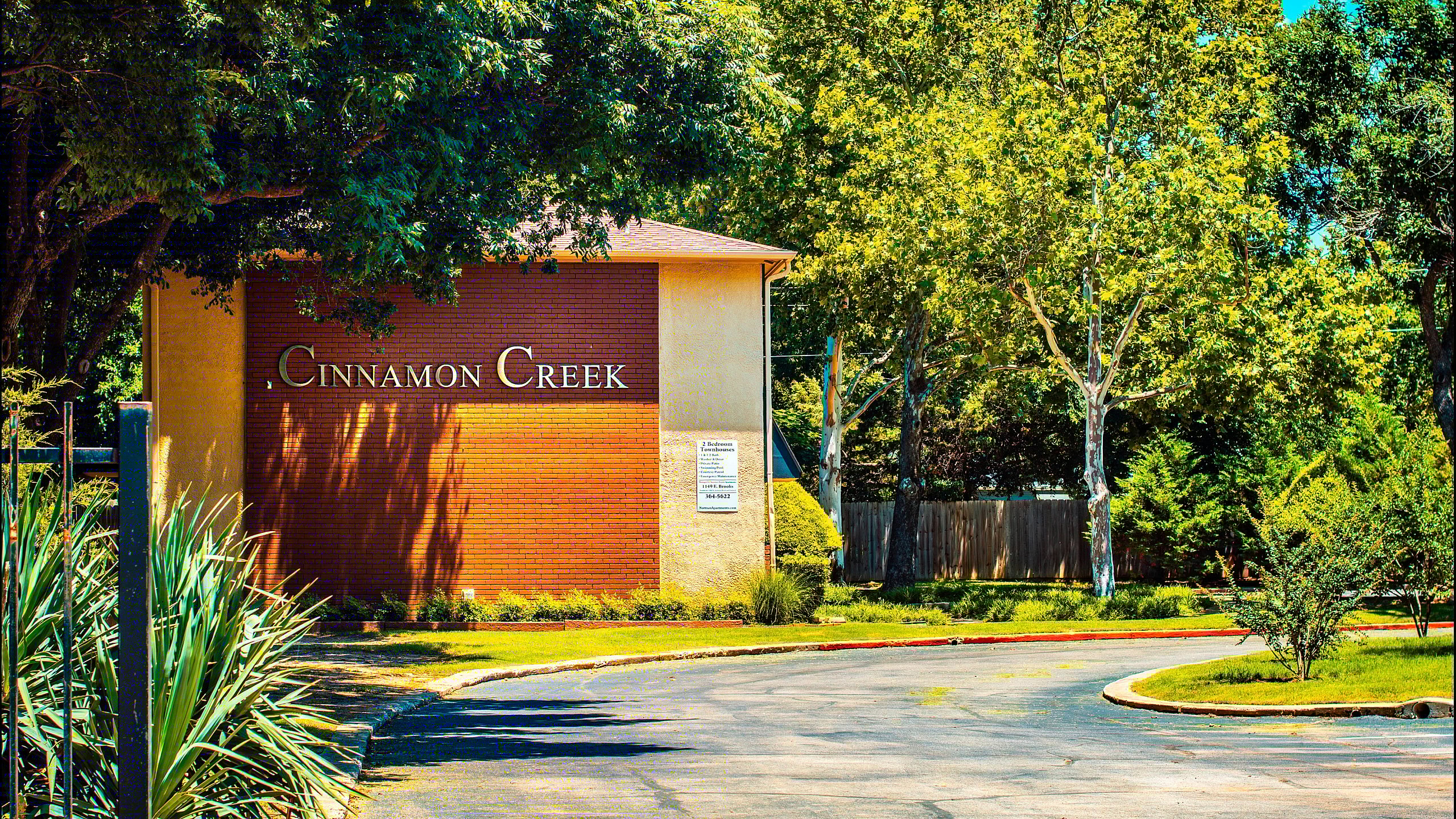 Inviting entrance of Cinnamon Creek apartment complex surrounded by lush greenery.