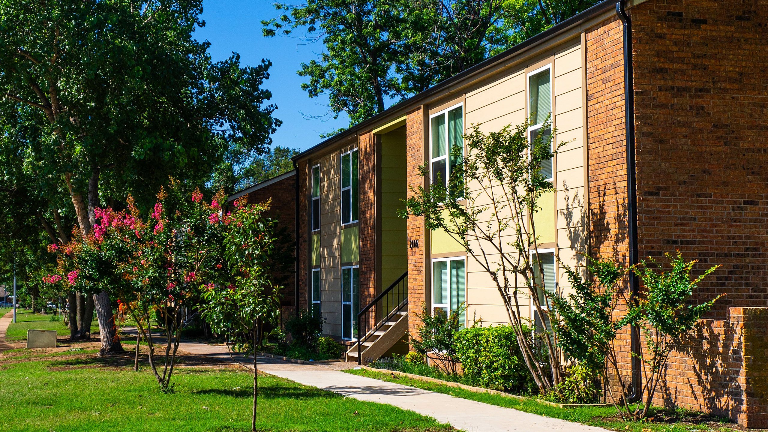 Picturesque exterior of a modern apartment building surrounded by lush trees and vibrant landscaping.